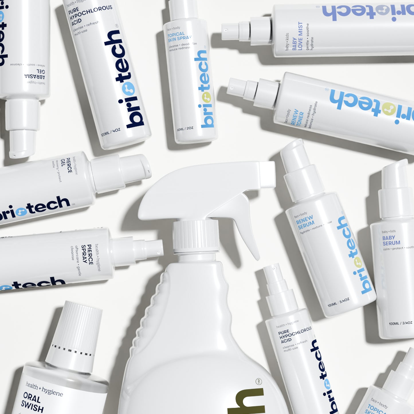 A selection of white “briotech” bottles, including the Renew Toner and a large facial mist spray, are arranged on a white surface along with products for calming redness and an oral swish.